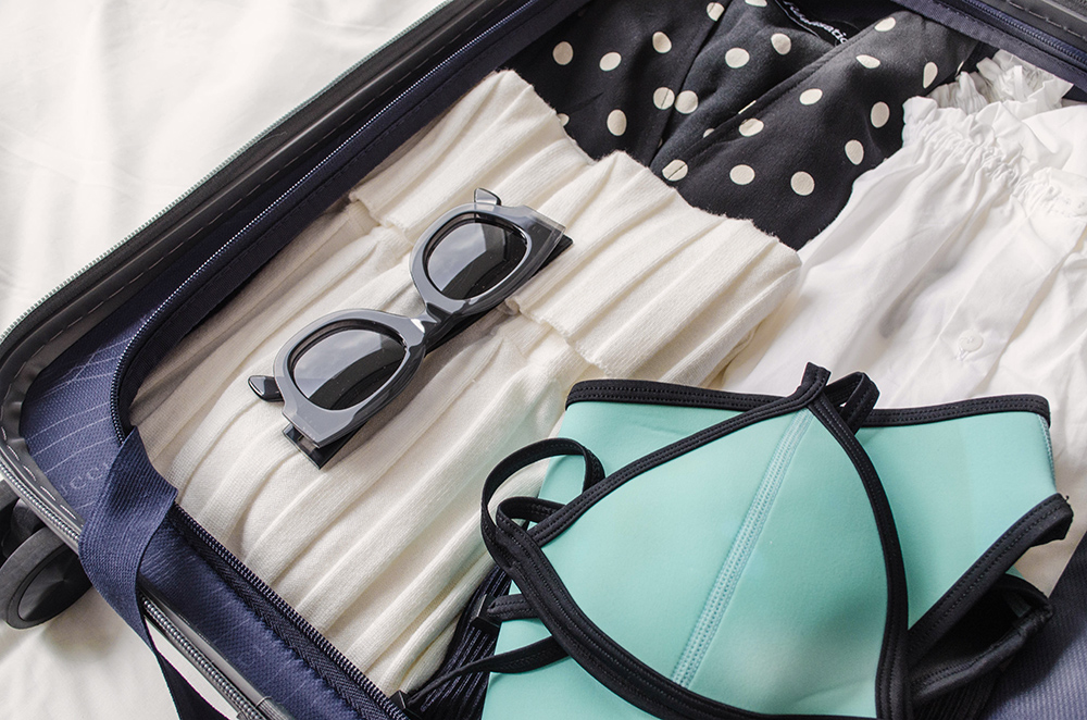 Packing suitcase for holiday. Triangle swimsuit and Celine sunglasses